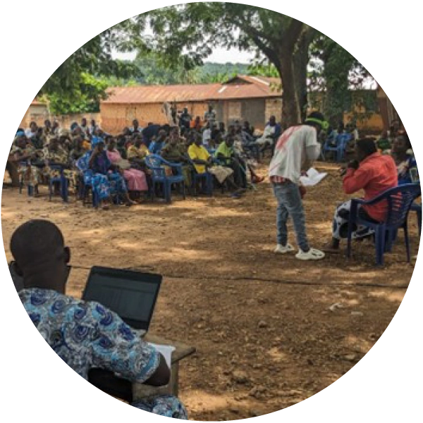 Round image of a speaker talking to a crowd outside