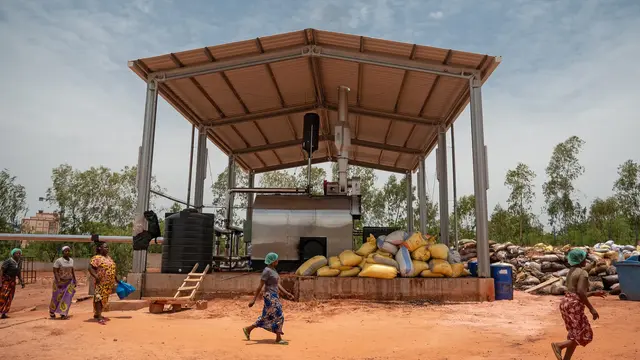 Workers in the outdoor area of the gebana factory in Burkina Faso; in the background, a covered facility for recycling cashew waste
