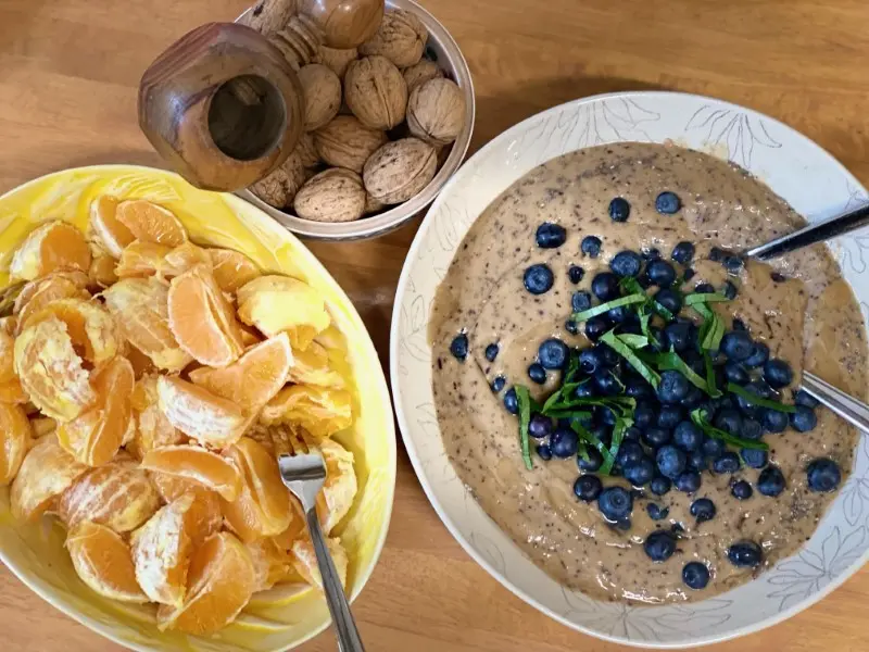Photo of three bowls, one filled with clementine slices, one with porridge and blueberries, one with walnuts, gebana.com