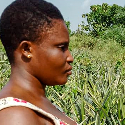 Profilansicht einer togolesischen Bäuerin mit kurzen Haaren vor grüner Naturlandschaft - gebana.com