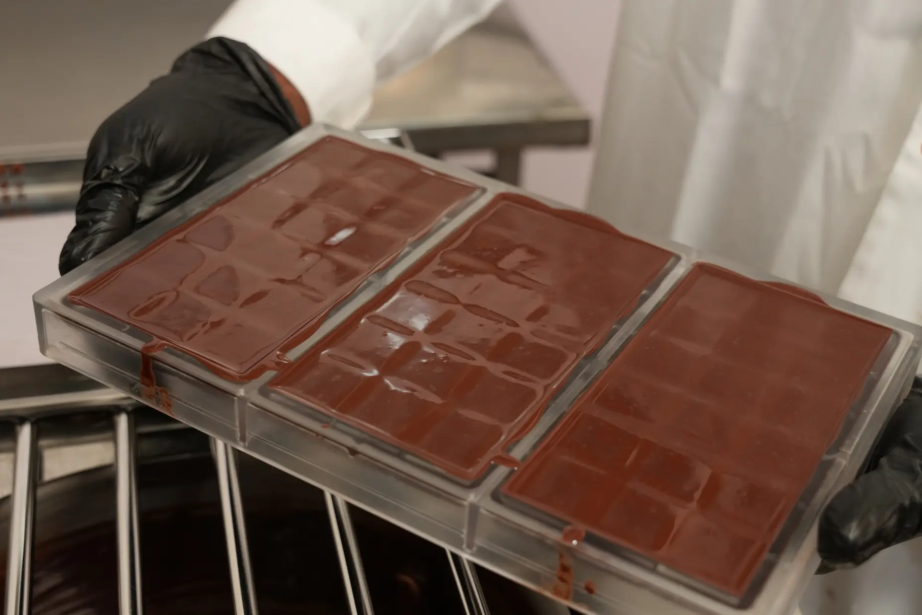 Foto von Händen die eine Form mit drei frisch gegossenen Schokoladetafeln halten - gebana.com