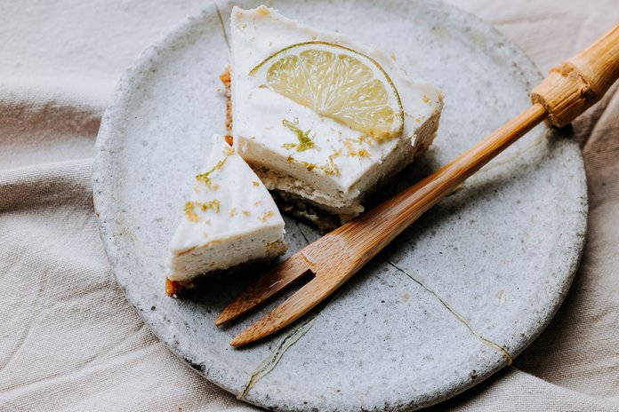 Stück eines Limetten-Cashew-Raw-Cake auf einem Teller mit Holzgabel - gebana.com